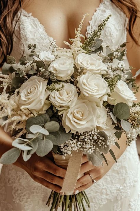 A bridal bouquet featuring white roses and feathery white astilbe mixed with eucalyptus greenery, held by a bride in a lace dress.