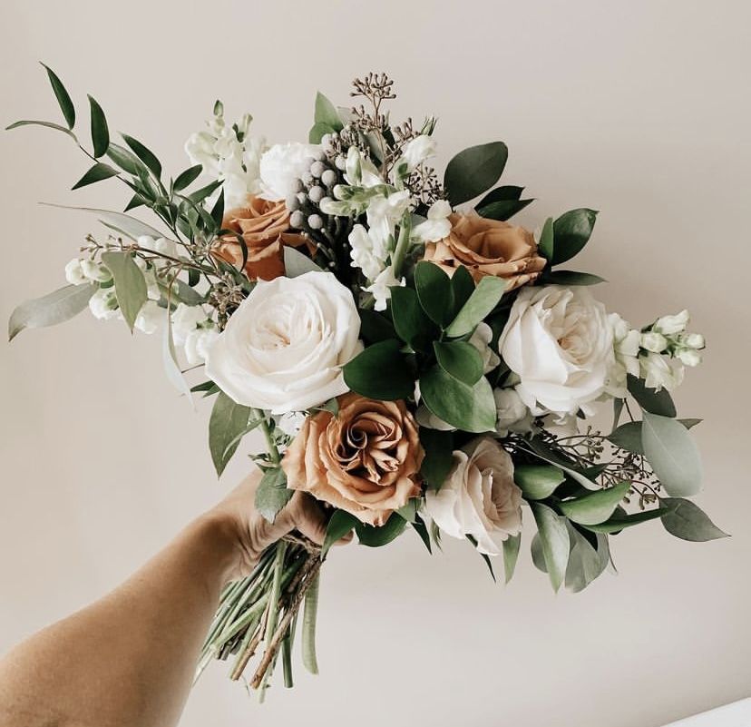 A contemporary bridal bouquet featuring white and toffee-colored roses with glossy dark green leaves and architectural foliage.