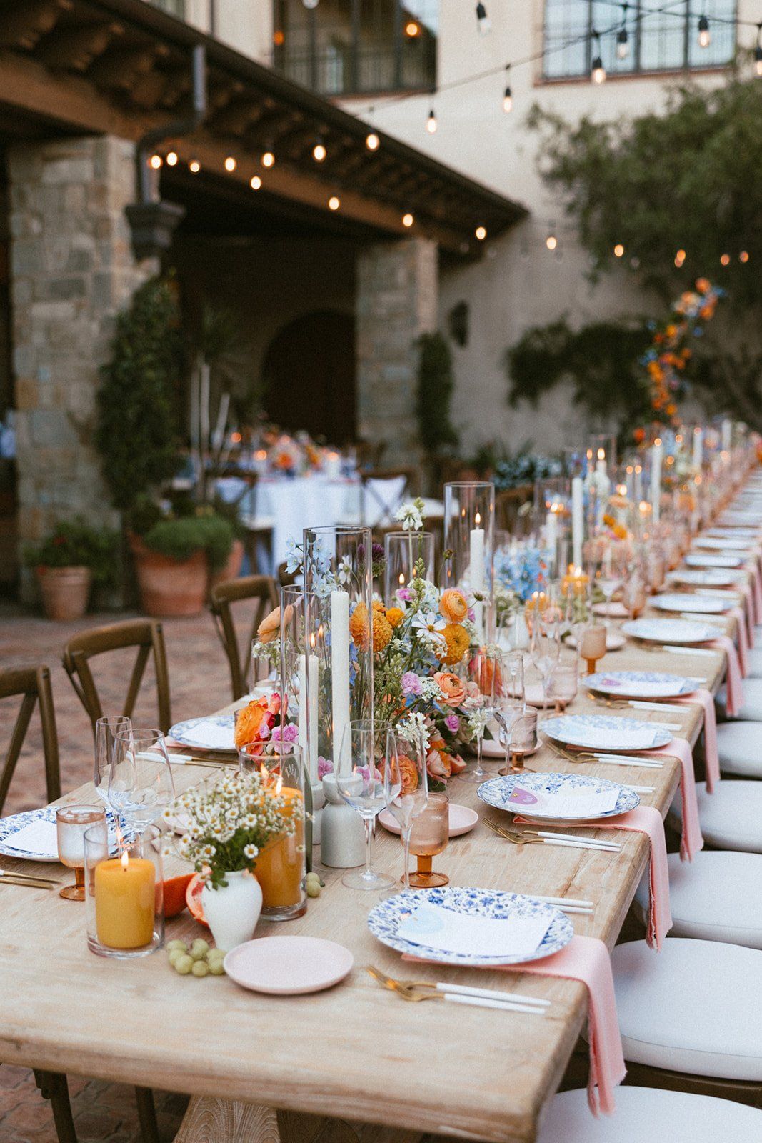 Long outdoor table with blue patterned plates, pink napkins, and fresh fruit accents.