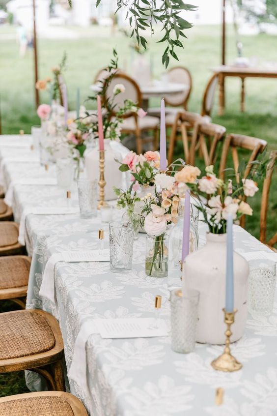 Table with blue leaf-patterned tablecloth and colorful tall tapered candles.