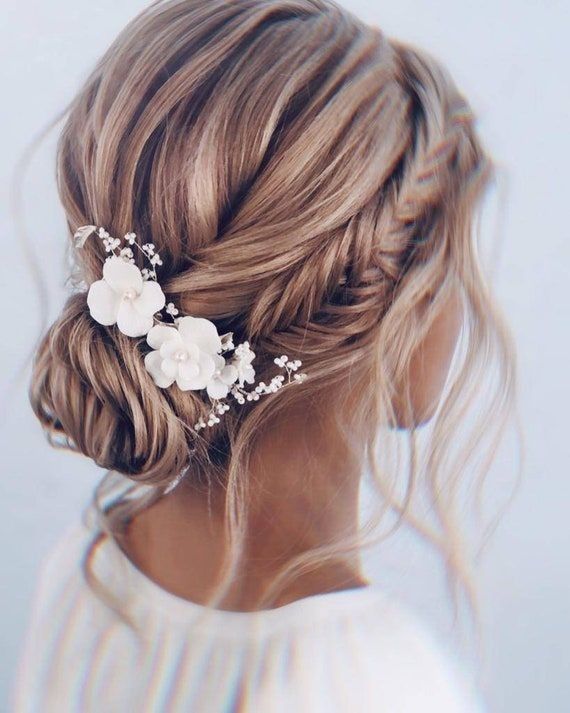 A bride with blonde hair in a textured low bun with white floral clips and soft waves.