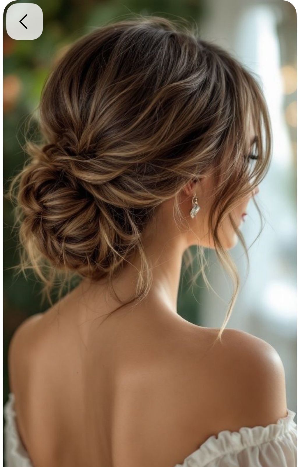 An effortless low tumbled bun on brunette hair with soft tendrils.