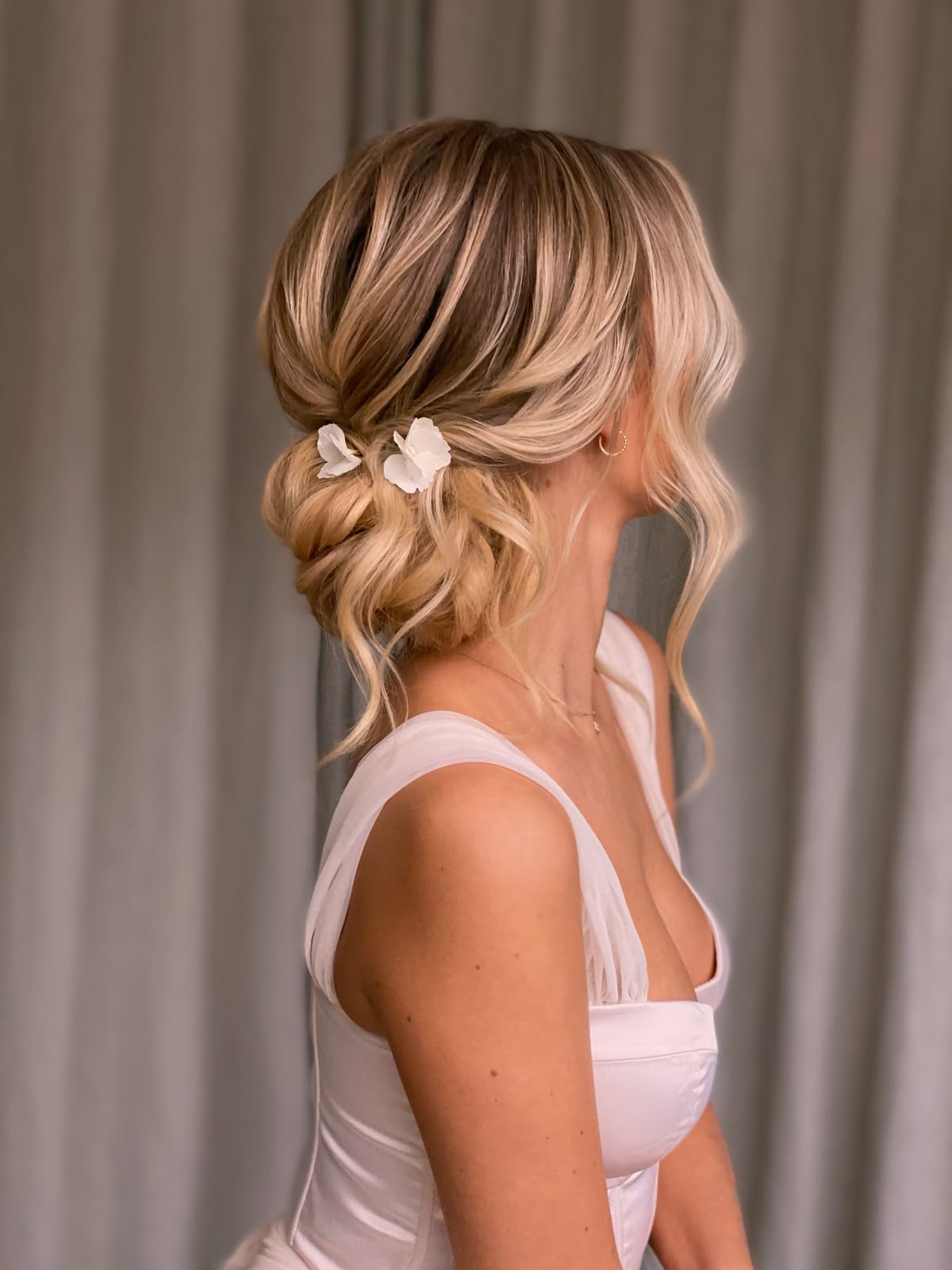 A soft chignon on blonde hair accented with delicate white floral petals.