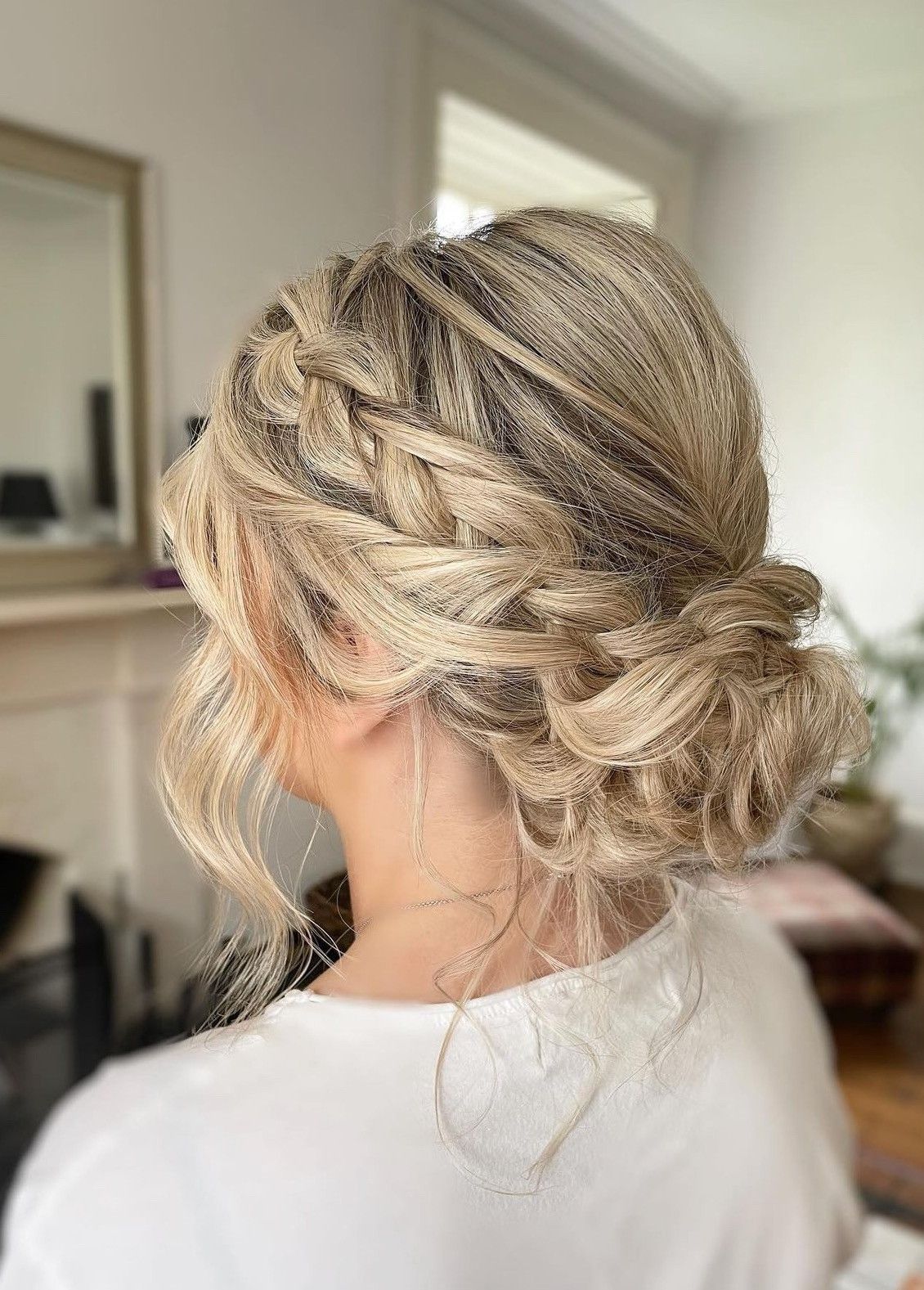 A thick side braid leading into a full, textured low bun on blonde hair.