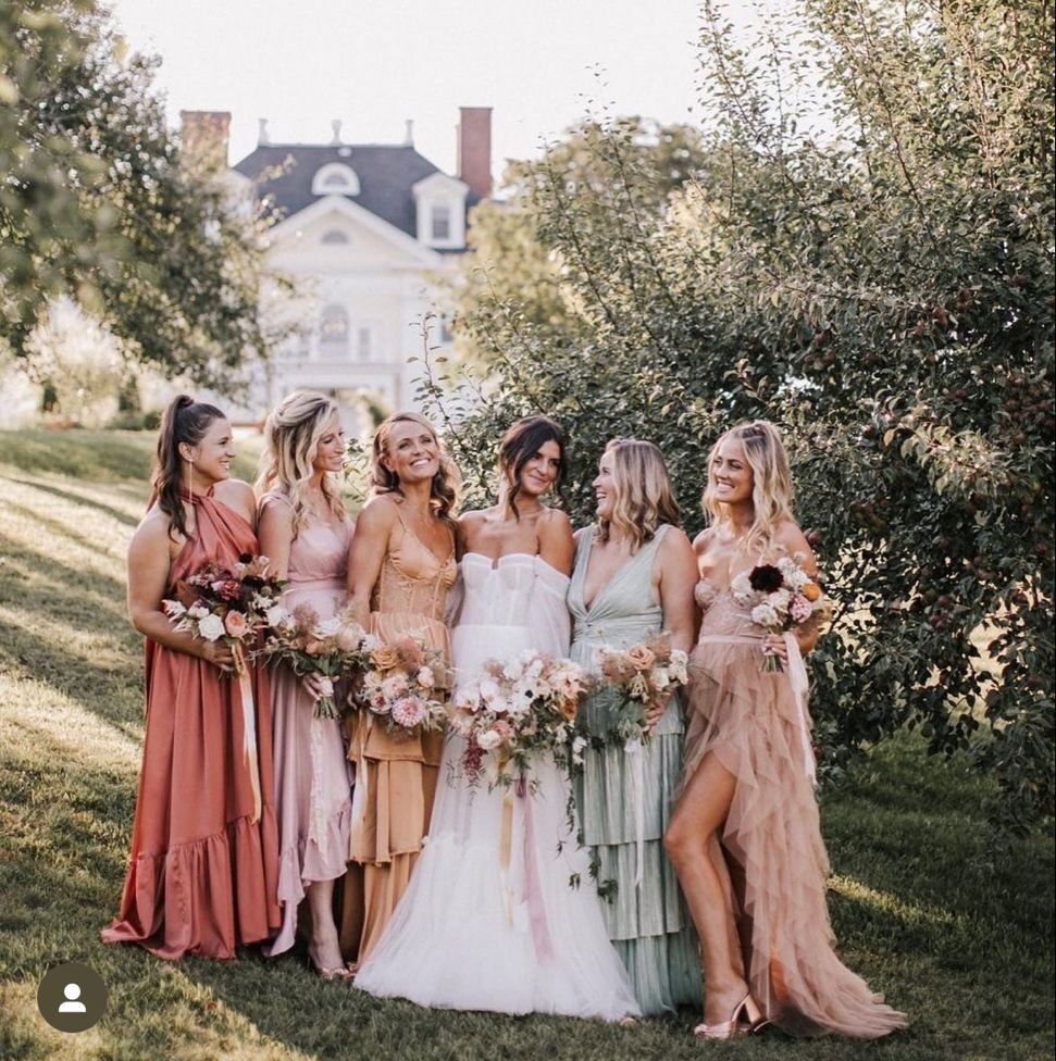 Bridesmaids standing in a field wearing a mix of dusty blue floral print dresses and solid blue gowns.