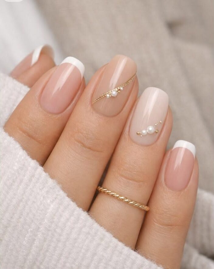 Short square French tip nails with gold line detailing and dainty pearl embellishments.
