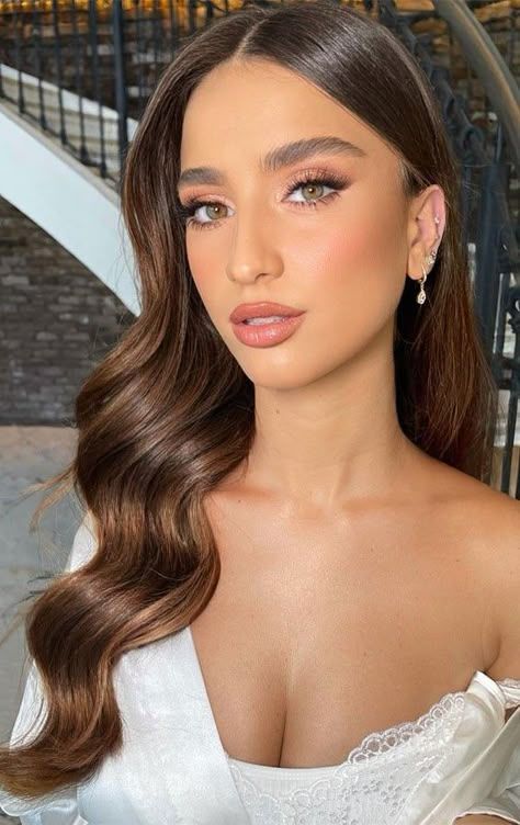 Glamorous woman with side-parted brunette hollywood waves and radiant makeup.

