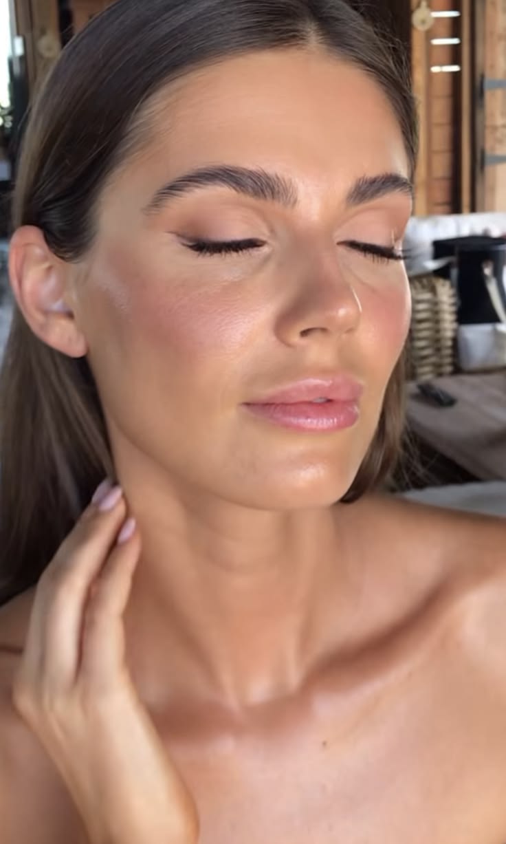 Close-up of a woman with glowing, natural makeup featuring soft brown eyeshadow, subtle winged eyeliner, dewy skin, and a nude glossy lip, creating a fresh and elegant bridal look.