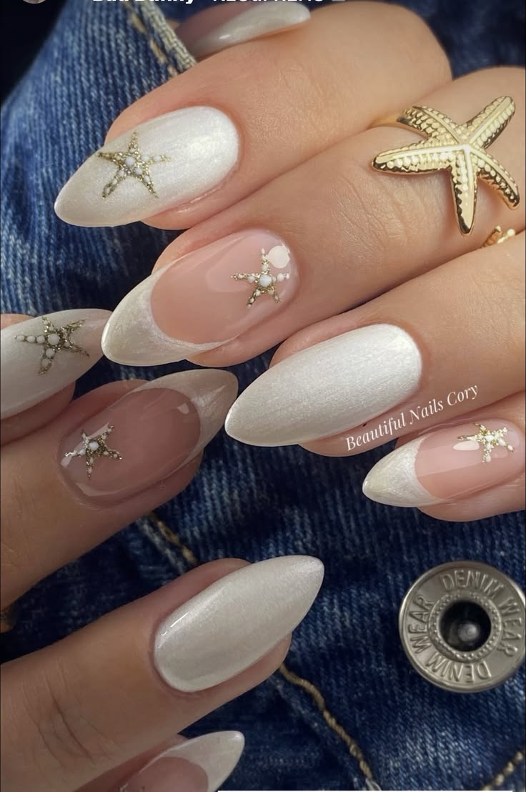 Pearlescent white chrome almond shaped nails with matching French tips, decorated with small gold starfish charms and white bead accents.