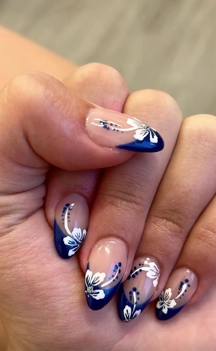 Almond shaped nails with deep royal blue French tips decorated with detailed hand painted white hibiscus flowers and dark blue stamen dots.