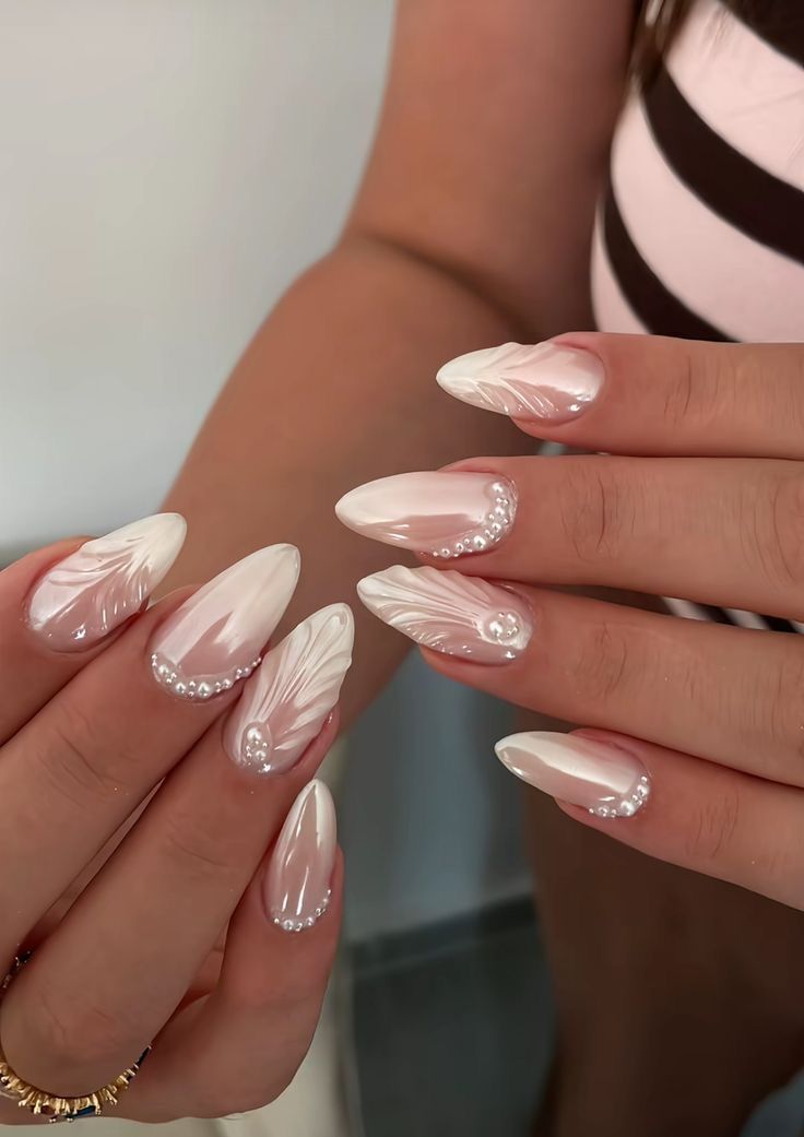 Long pointed almond shaped nails with a shimmering pearlescent white finish, featuring elegant 3D seashell ridges and clusters of tiny white pearls near the cuticles.