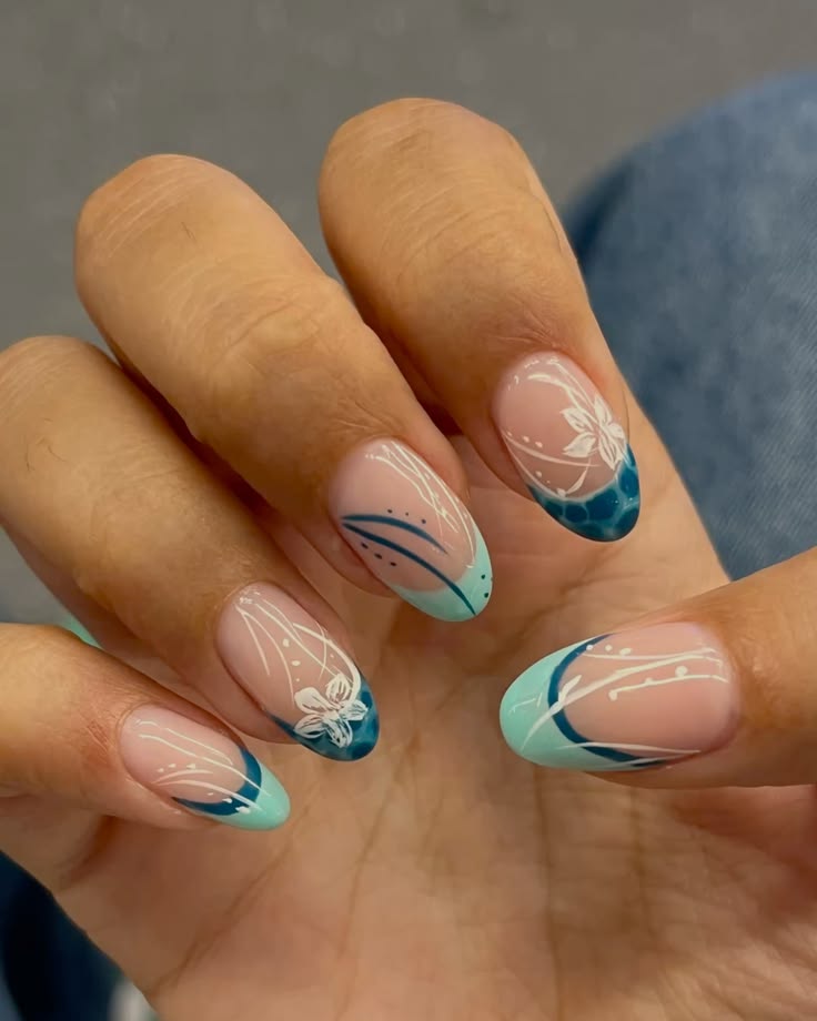 Long almond shaped nails with a clean nude base and clear-to-blue ombré French tips, decorated with delicate white linework and hand painted white flowers.

