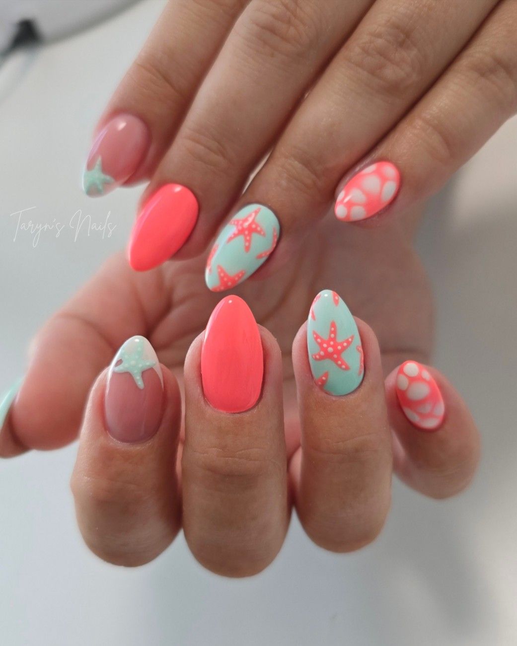 Long almond shaped nails featuring alternating solid coral and mint green polish with a white starfish accent design.