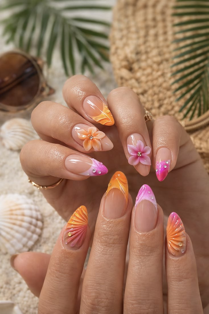Pointed almond shaped nails featuring orange and pink ombré French tips, 3D tropical flowers with rhinestones, and textured seashell patterns.