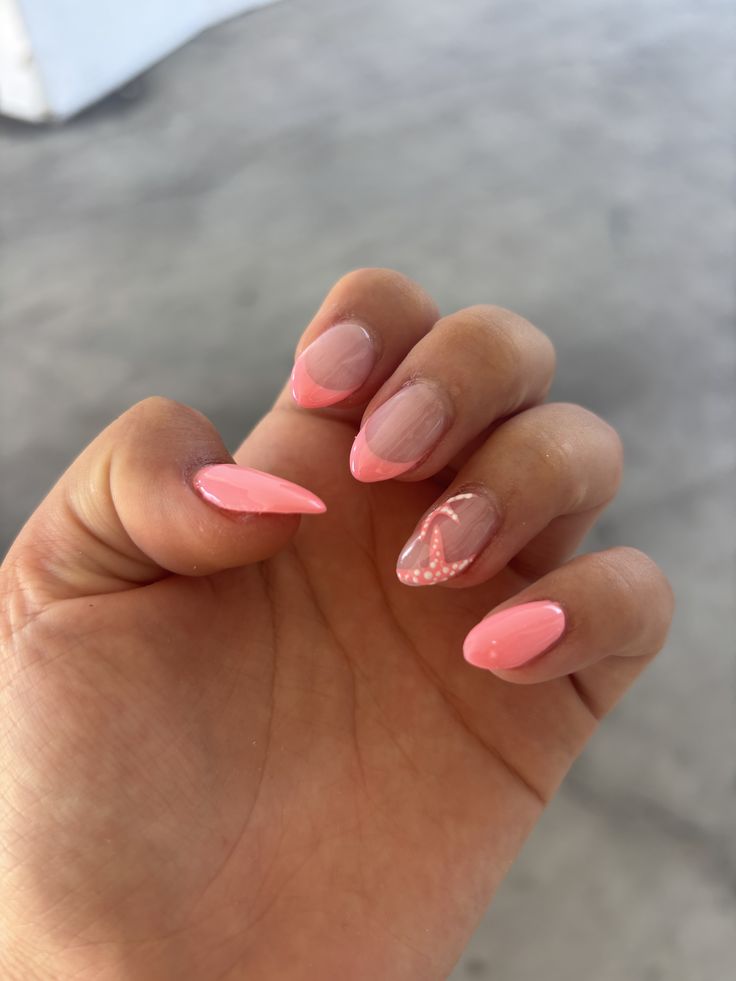 Almond shaped nails with soft coral pink polish, including matching French tips and an accent nail with a white dotted starfish design.