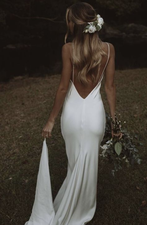 Back view of a bride walking through a grassy field wearing a smooth white silk low-back slip wedding dress with a flower hair clip.
