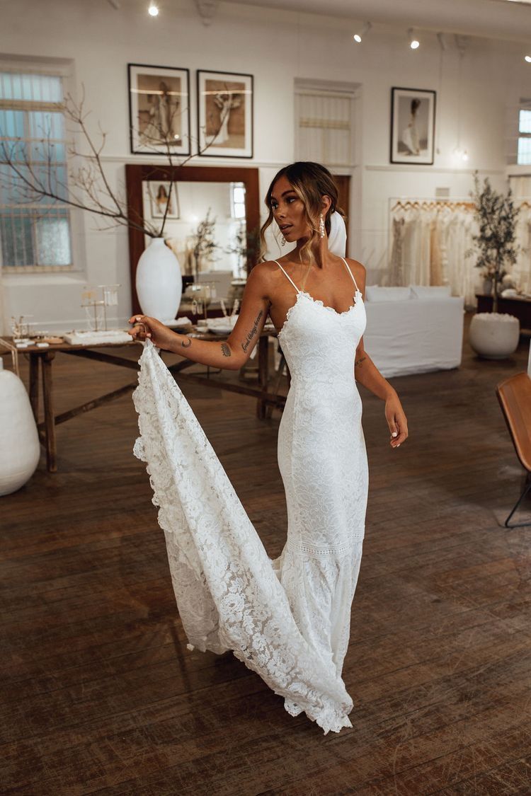 Bride looking over her shoulder in a bridal boutique wearing a fitted white eyelash lace mermaid wedding dress with a detailed train.