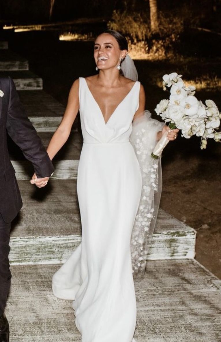 Close up of a bride walking at night wearing a structured white wedding gown with a deep V neckline and holding white flowers.