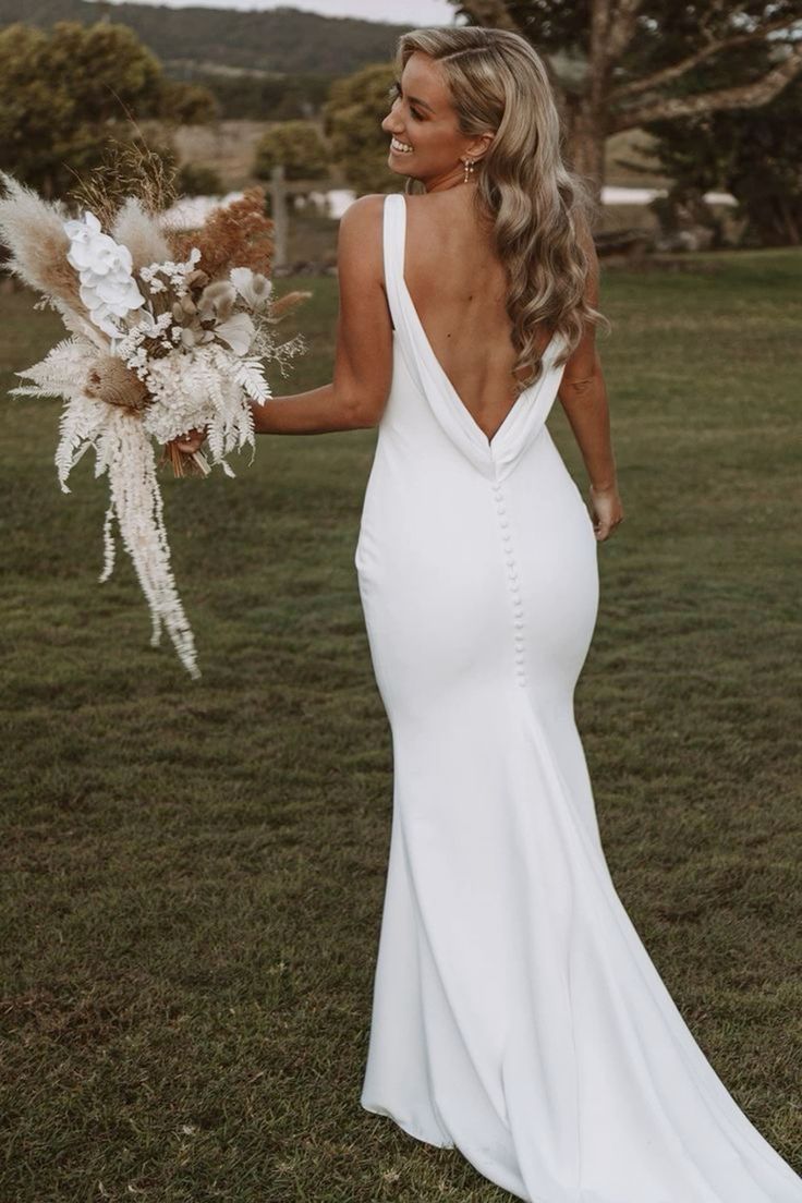 Back view of a bride with long wavy blonde hair wearing a white crepe wedding dress with a low draped cowl back and buttons.