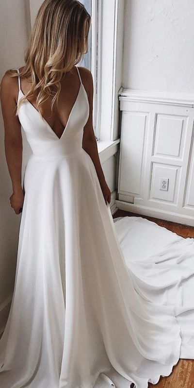 Side profile of a white A lined wedding dress with a deep plunge neckline and thin straps next to a window.