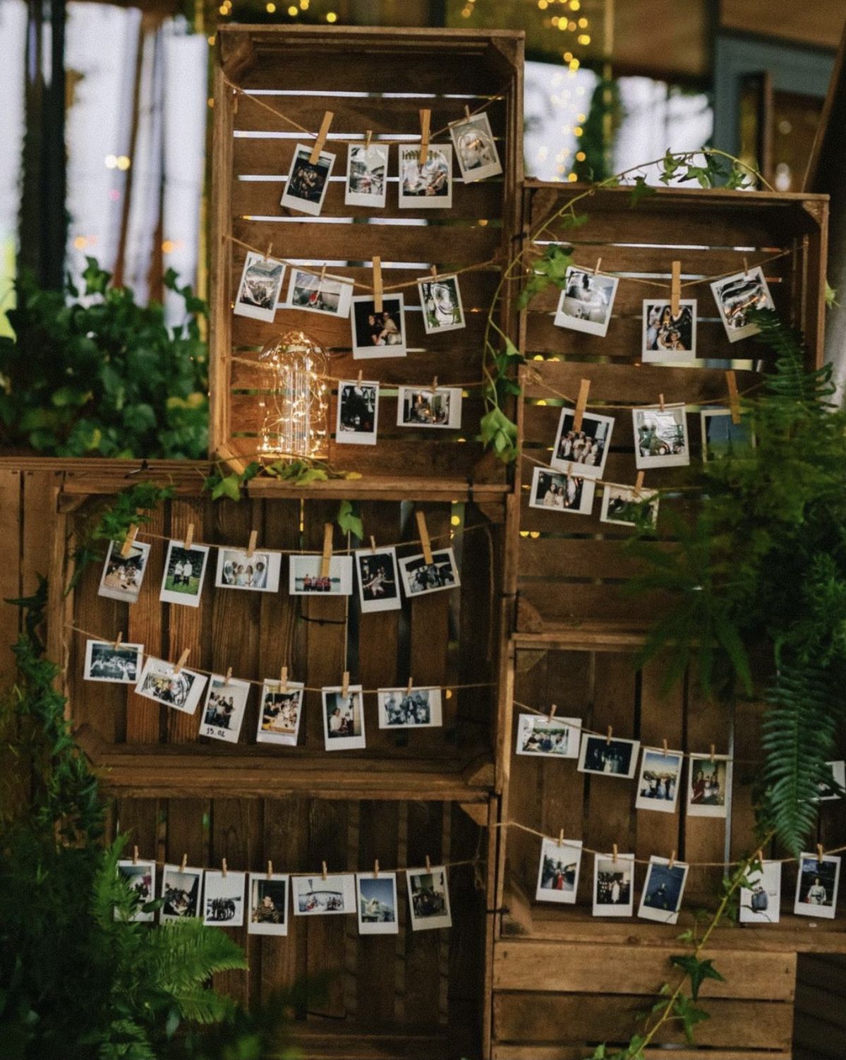 A wedding guest photo display wall built from stacked wooden crates with twine string lines holding hanging Polaroid pictures.