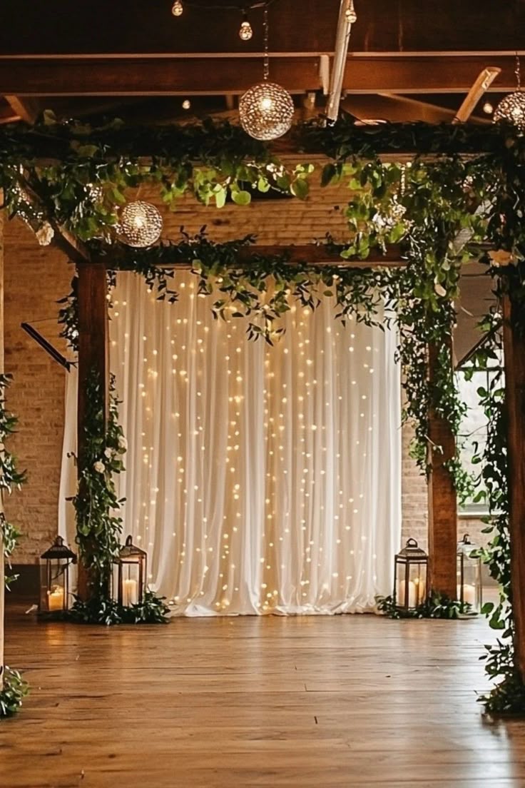 An indoor wedding backdrop featuring a white curtain covered in a waterfall of fairy lights and surrounded by thick green vines.