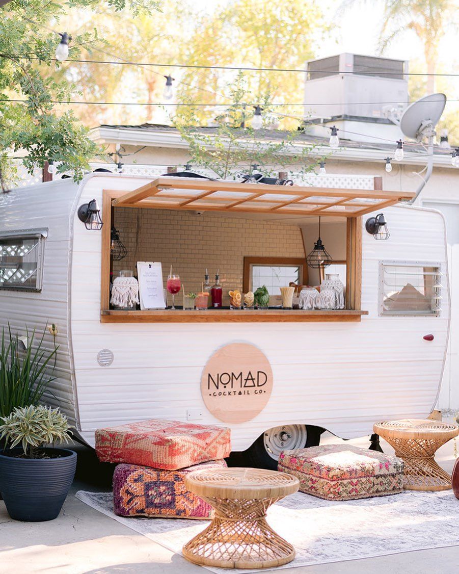 Boho caravan mobile bar with colorful floor cushions, rattan furniture, and relaxed outdoor lounge.

