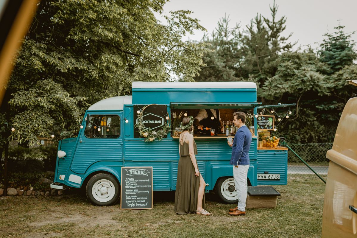 A bright blue vintage cocktail van with festoon lighting, a chalkboard menu, and a fresh citrus display.
