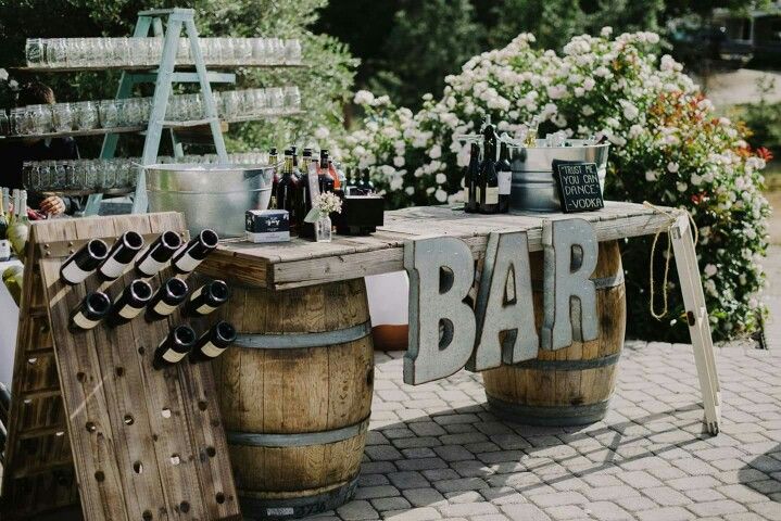 Rustic wine barrel bar with metal BAR letters, a wine bottle riddling rack, and a vintage glass ladder display
