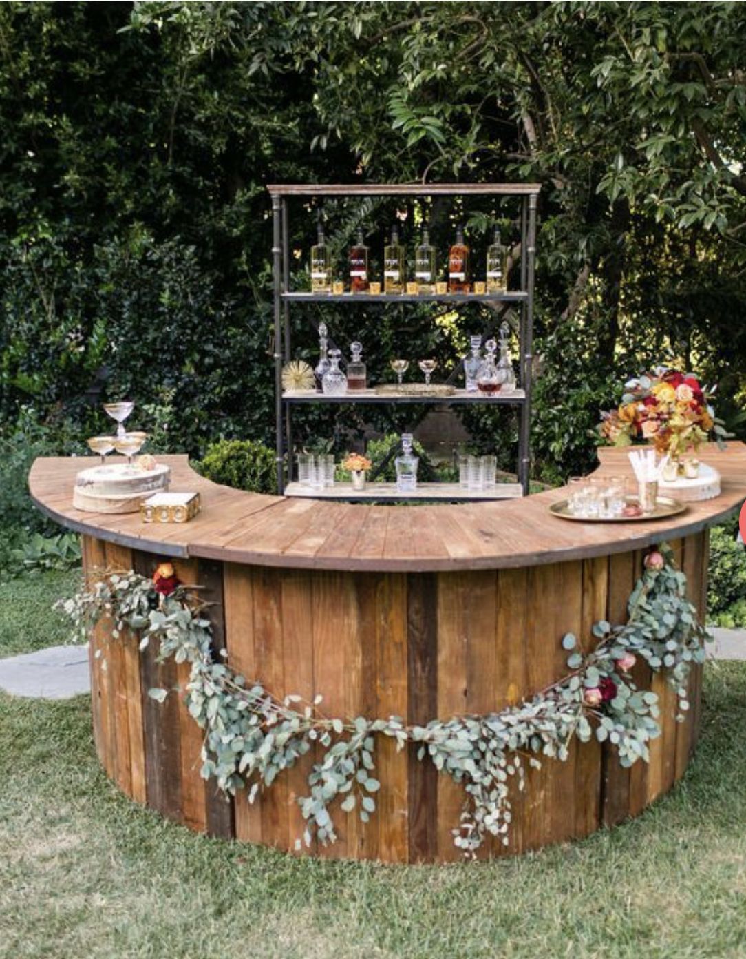 Curved wooden bar counter made from vertical planks, decorated with a eucalyptus garland and rustic wood slices
