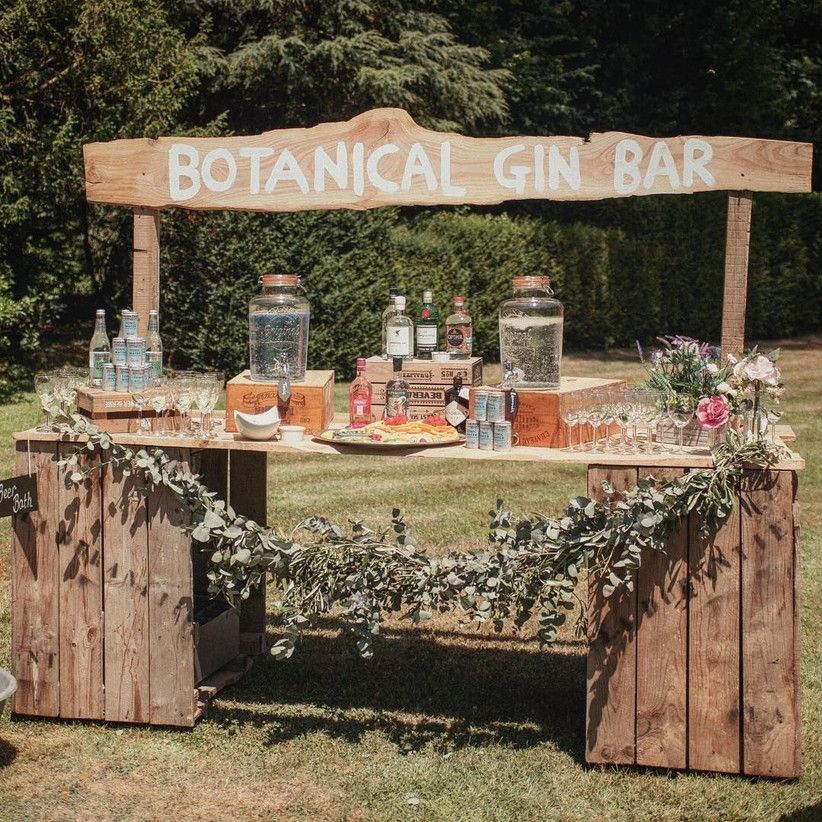 Wide outdoor wooden bar illuminated by suspended string lights and lanterns on an open lawn at dusk
