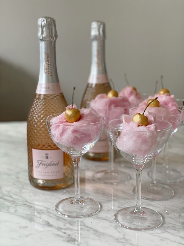 Champagne coupe glasses filled with pink cotton candy topped with sparkling rosé bottles.