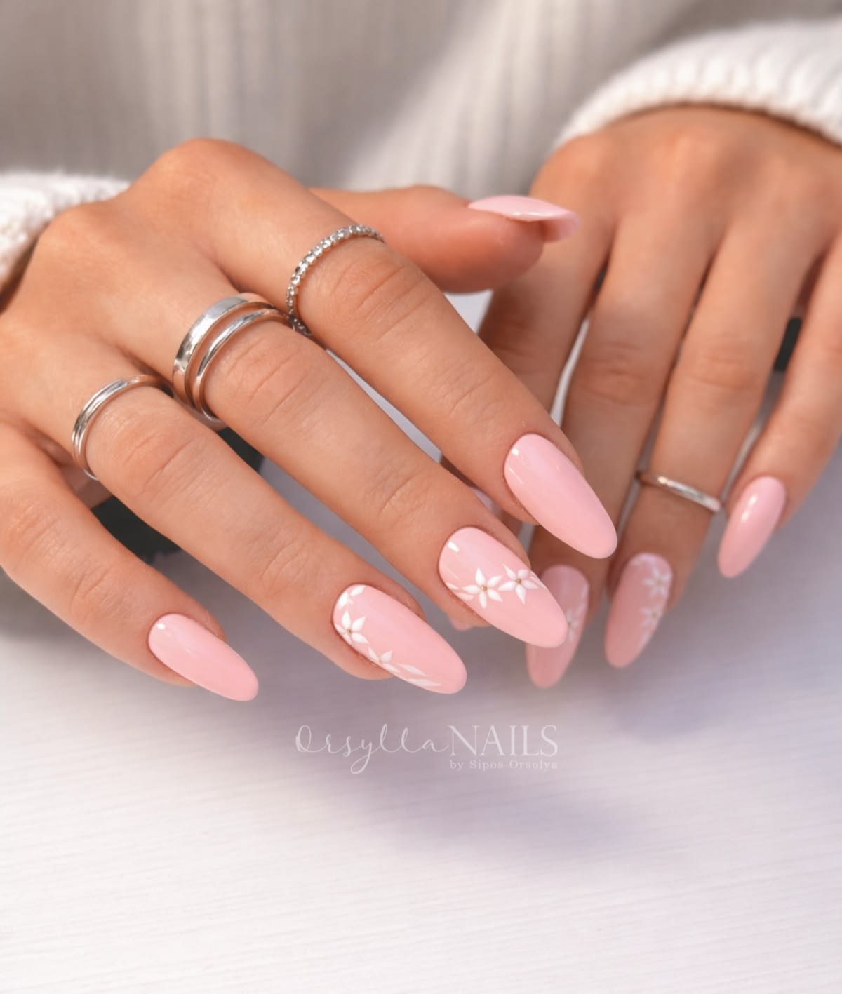 Classic pink summer manicure with hand-painted white floral vine accents and silver rings.