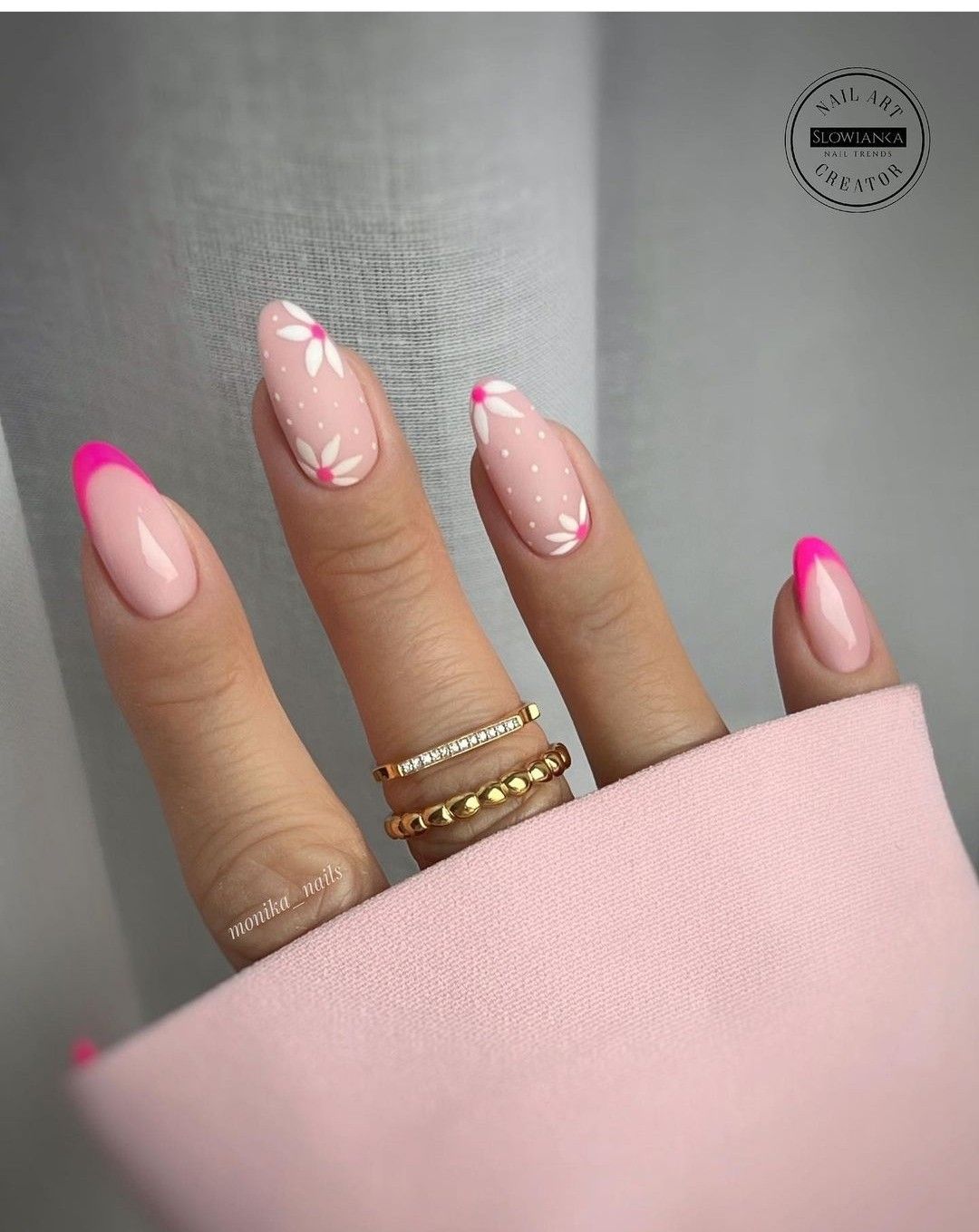 Soft pink almond nails featuring fuchsia French tips and white daisy nail art, holding a pink fabric.