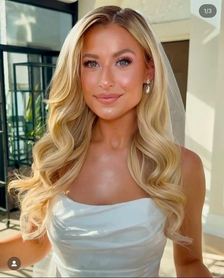 Bride with long bouncy waves parted in the center with a sheer veil pinned back. 