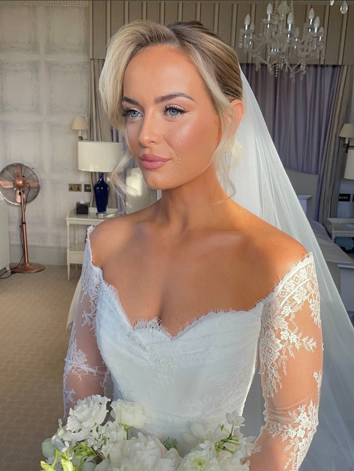 Bride with elegant, high blonde updo and soft tendrils wearing lace off shoulder dress. 