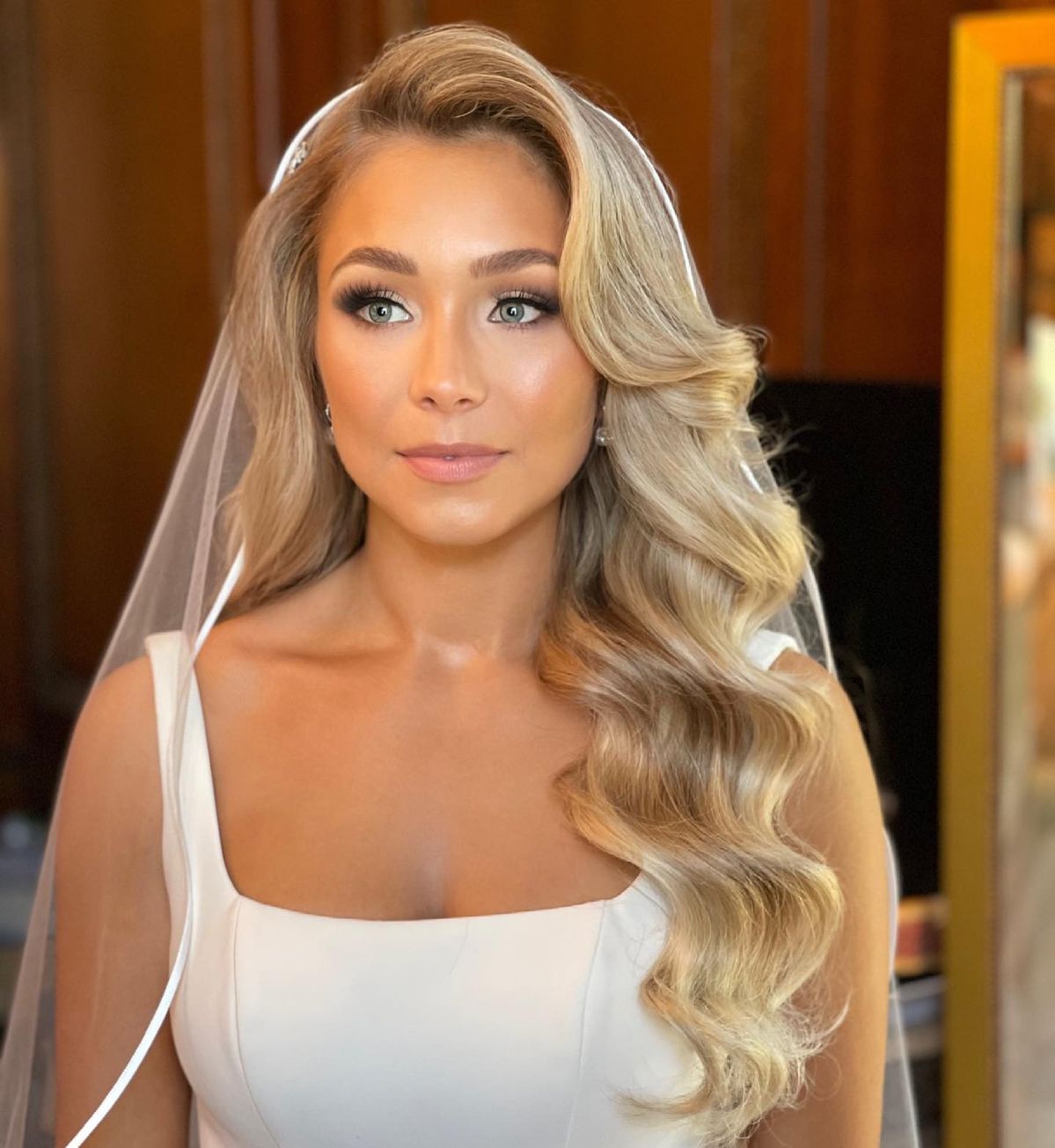 Bride with voluminous modern glam waves swept over one shoulder with a sheer veil. 
