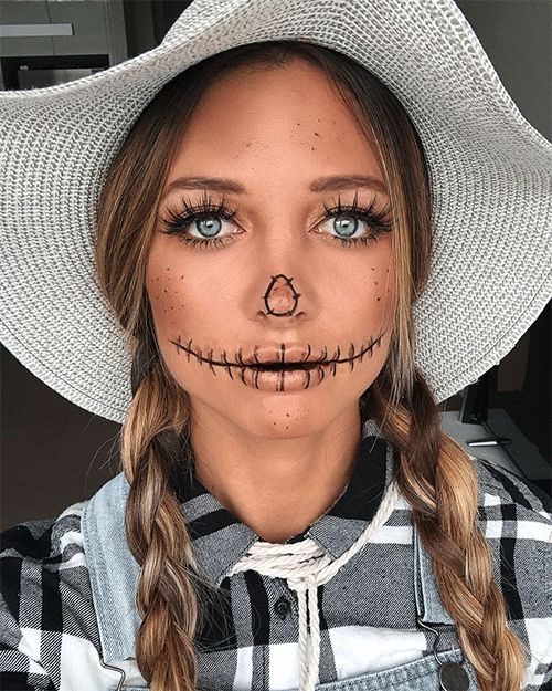 Woman wearing classic scarecrow Halloween makeup with stitched mouth details, braided hair and a straw hat