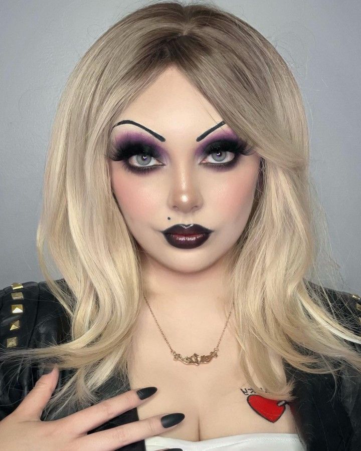 Woman wearing dramatic doll Halloween makeup with arched brows, purple smoky eyes and a dark ombré lip