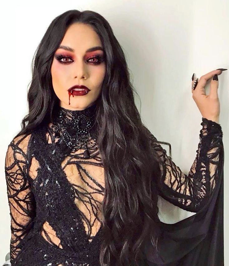 Woman wearing glamorous vampire Halloween makeup with cranberry eyeshadow, dark red lips and faux blood