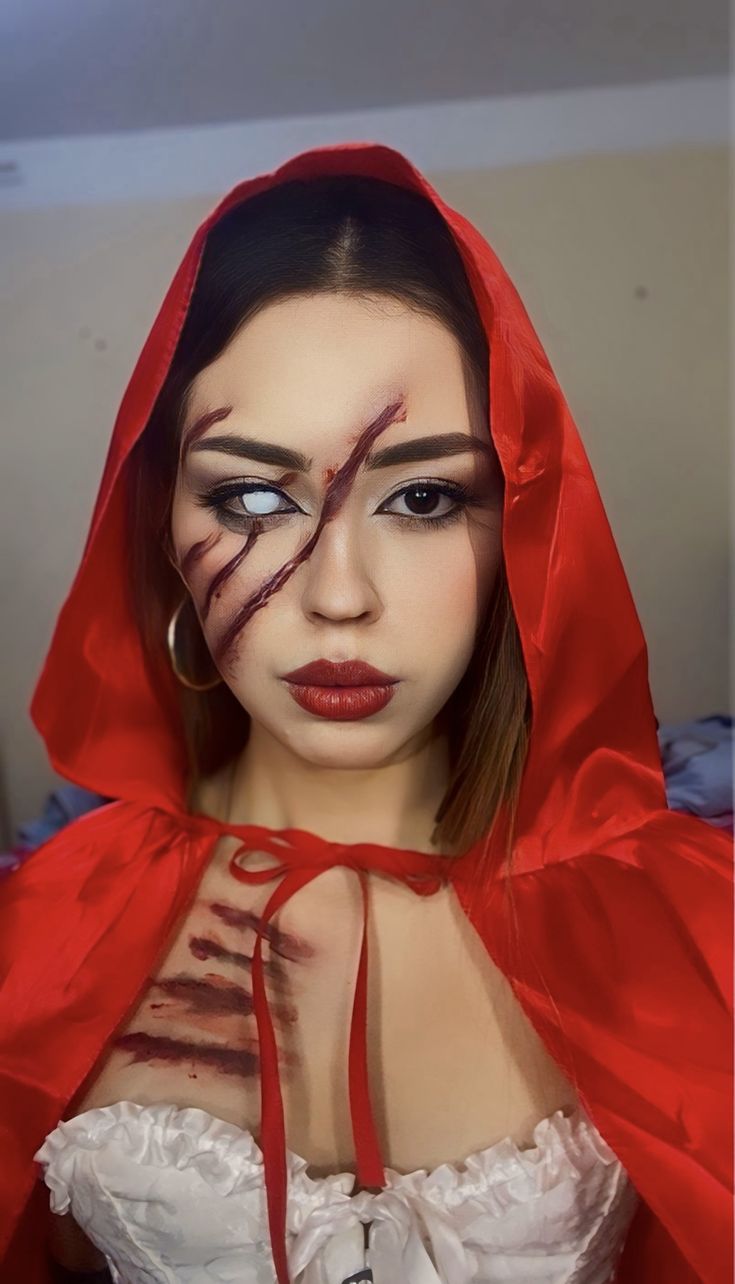 Woman dressed as Little Red Riding Hood with textured claw scratches across her face and red satin cape 
