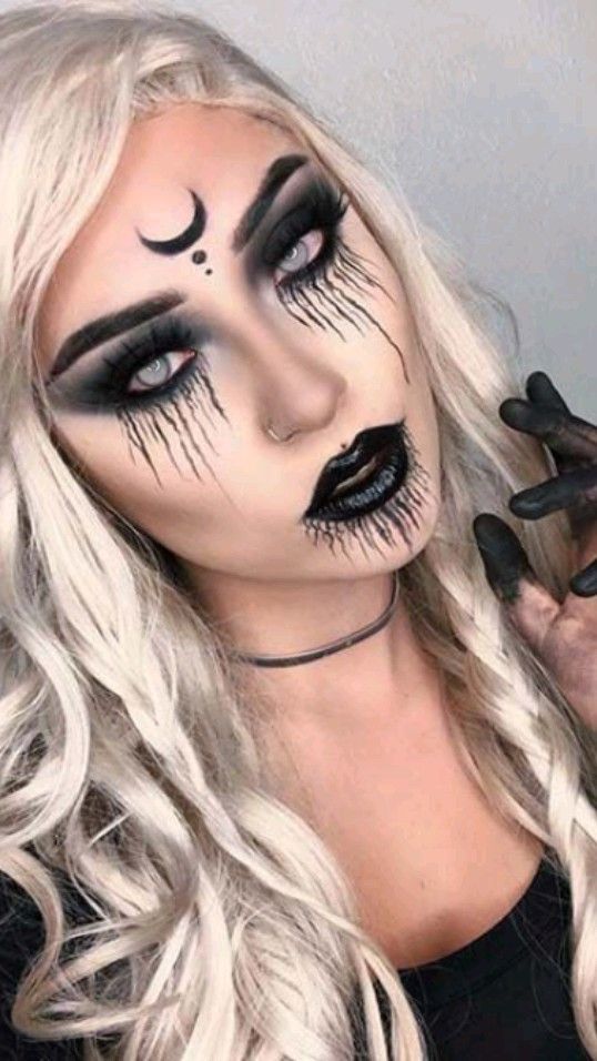 Woman with platinum blonde hair, a crescent moon forehead symbol, and dripping black tear makeup 
