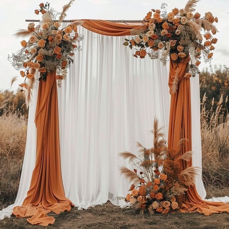 Outdoor wedding ceremony arch with rust-colored draping, white curtains, burnt orange roses, and pampas grass.
