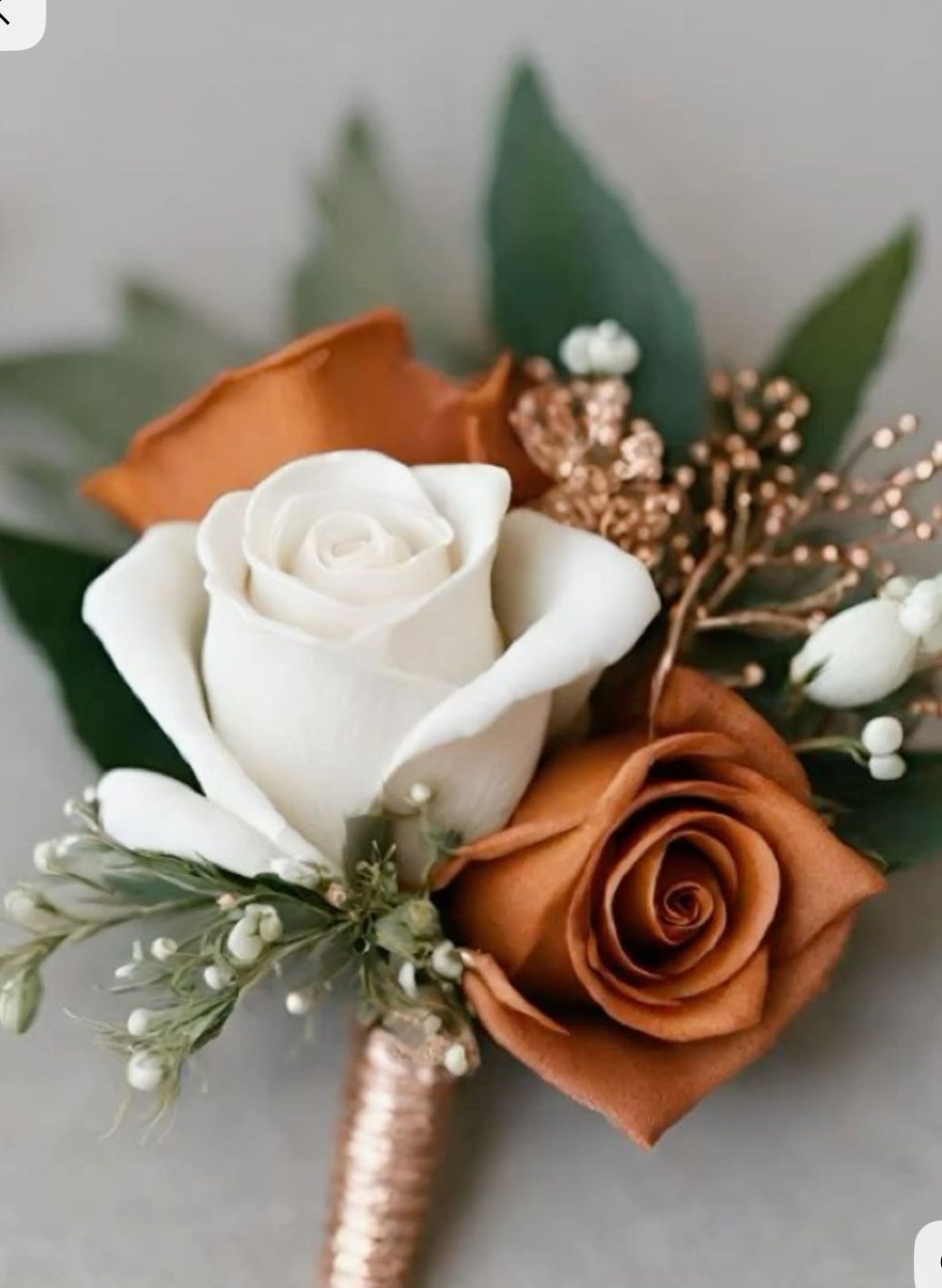 Wedding buttonhole featuring cream and rust roses, white buds, greenery, and copper-colored stem wrapping.