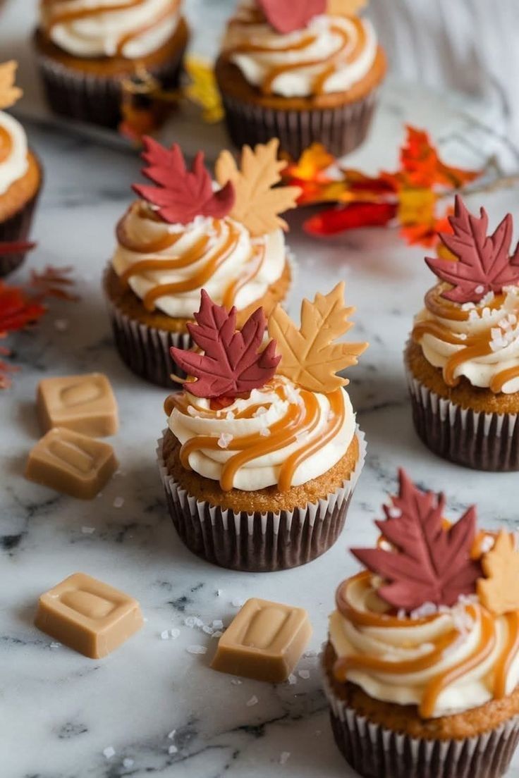 Autumn cupcakes topped with cream frosting, caramel drizzle, and decorative red and gold leaves.