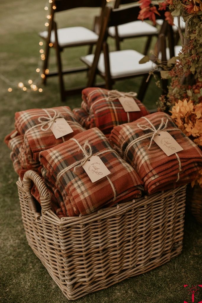 A wicker basket filled with rust and cream plaid blankets tied with twine and tagged for wedding guests.