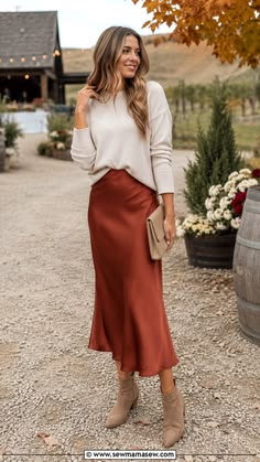 Woman wearing a rust satin midi skirt with a cream sweater at a fall wedding venue
